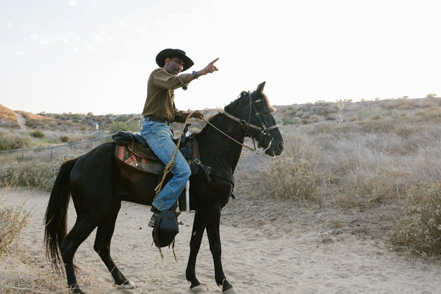 Person on horseback pointing ahead, wearing a cowboy hat and jeans, riding through a dry, brushy landscape.